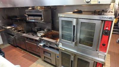 Deep fryers, salamander, griddle, and stacked Vulcan convection ovens on cook line